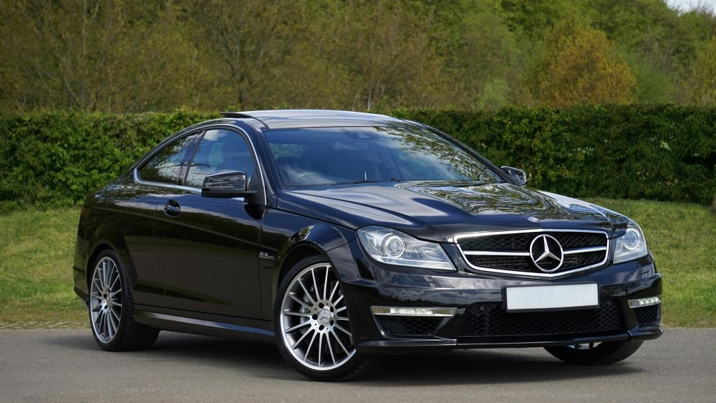 Luxurious black Mercedes Benz coupe parked on a scenic outdoor setting with lush greenery.